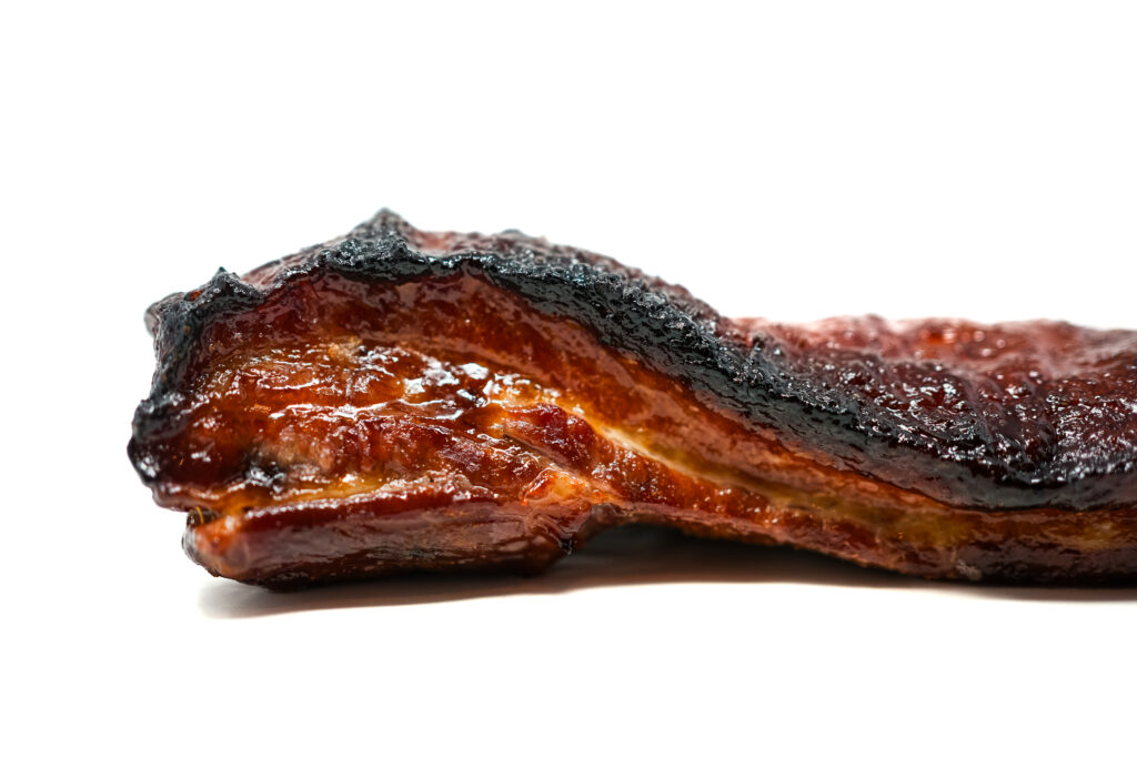 A slice of Momofuku-inspired pork belly with a mahogany-colored caramelized exterior, visible layers of tender meat and rendered fat, glistening with the sweet-savory glaze characteristic of the famous restaurant recipe.