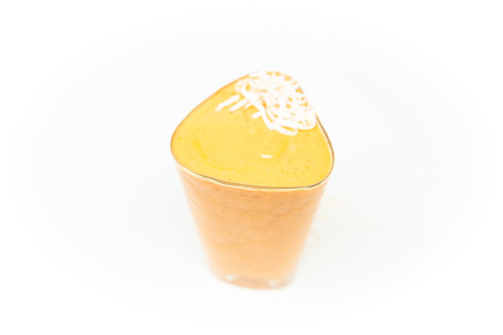 A creamy orange papaya coconut fig smoothie served in a clear glass, topped with shredded coconut on a white background.