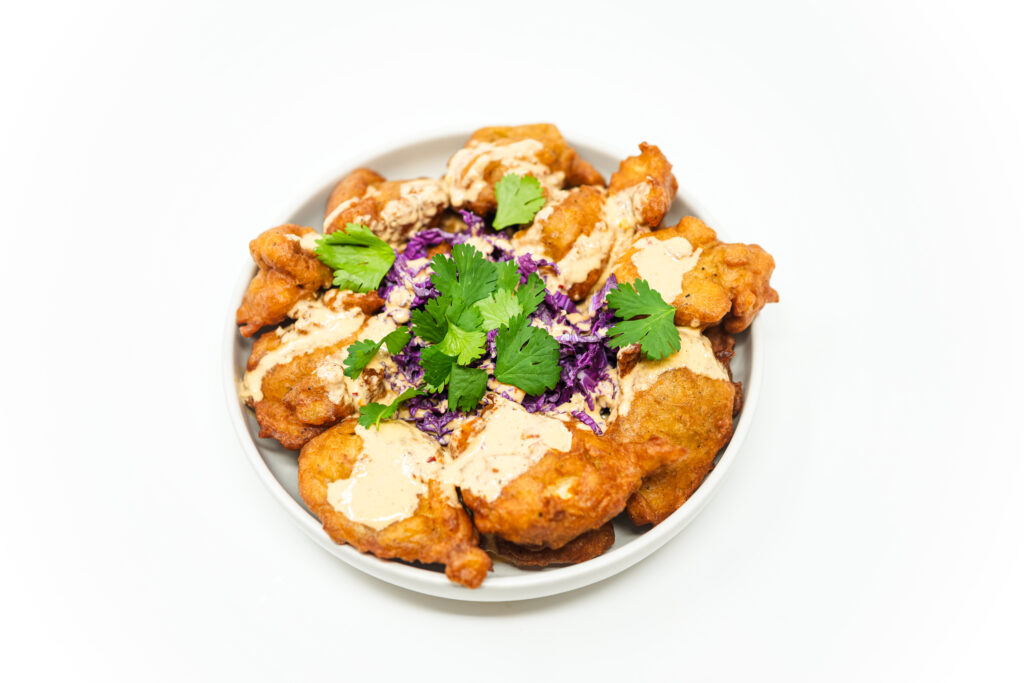 Crispy yuca fritters served alongside purple cabbage and fresh cilantro, drizzled with zesty horseradish sauce for a vibrant and flavorful presentation.