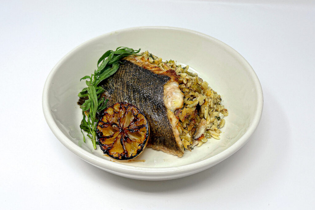 Herb and Orzo Stuffed Flounder, featuring tender flounder fillets filled with a flavorful orzo and herb stuffing, served with a light garnish of tarragon and lemon wedges for a fresh, vibrant presentation.