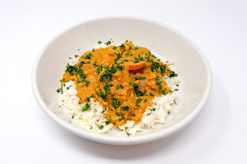 A bowl of Coconut, Carrot, and Cauliflower Curry served over fluffy rice, garnished with fresh cilantro, showcasing the creamy coconut broth, tender vegetables, and vibrant colors.