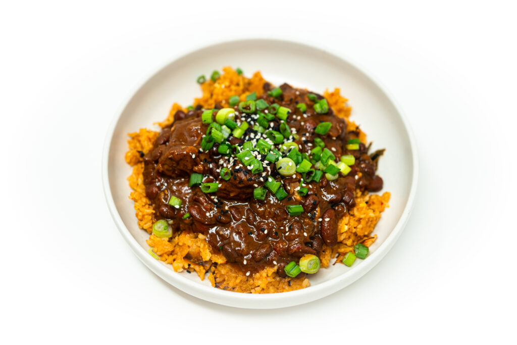 A bowl of Korean BBQ-inspired beef chili over kimchi fried rice, topped with green onions and a drizzle of sesame oil.