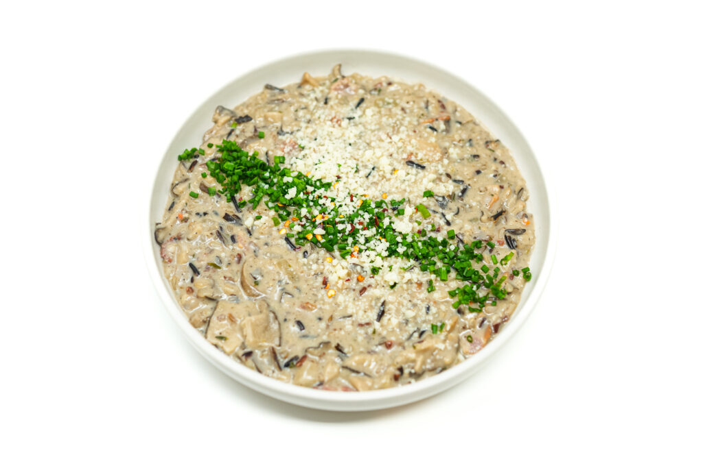 A bowl of Mezcal-Infused Creamy Mushroom and Wild Rice Soup, featuring golden-brown shiitake mushrooms, wild rice, and crispy bacon in a rich, creamy broth, garnished with chopped chives and Parmesan cheese.