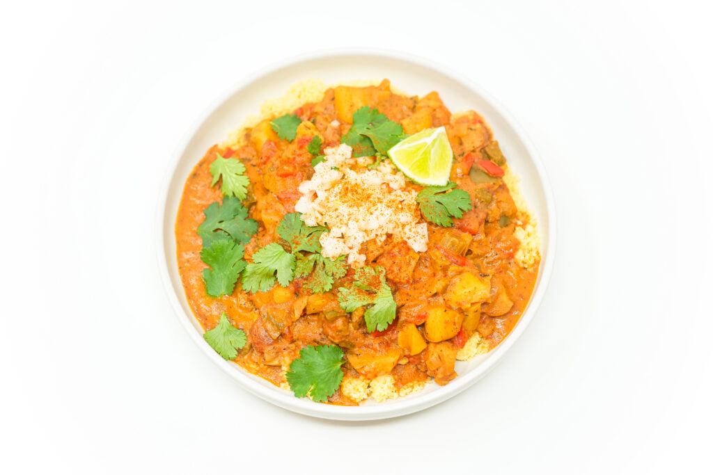 A vibrant bowl of Caribbean-Inspired Conch Chowder, featuring tender conch pieces, colorful vegetables, and a rich coconut milk-based broth, garnished with fresh cilantro and diced onion.
