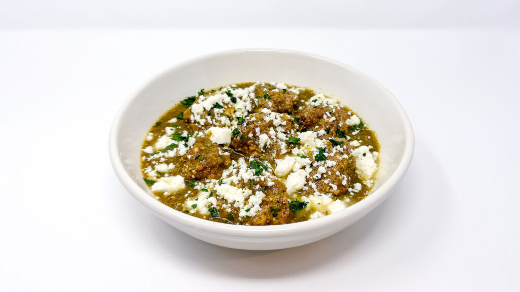 Tomatillo queso fresco meatballs served in a bowl, topped with fresh cilantro and drizzled with a tangy tomatillo sauce, showcasing the juicy meatballs and creamy queso fresco.