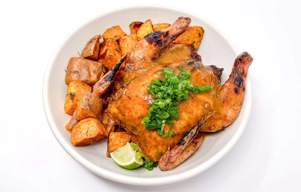 A beautifully roasted Mango-Tamarind Glazed Cornish hen served on a plate, glistening with a rich, caramelized glaze, and garnished with fresh herbs, showcasing its golden, crispy skin and juicy interior.