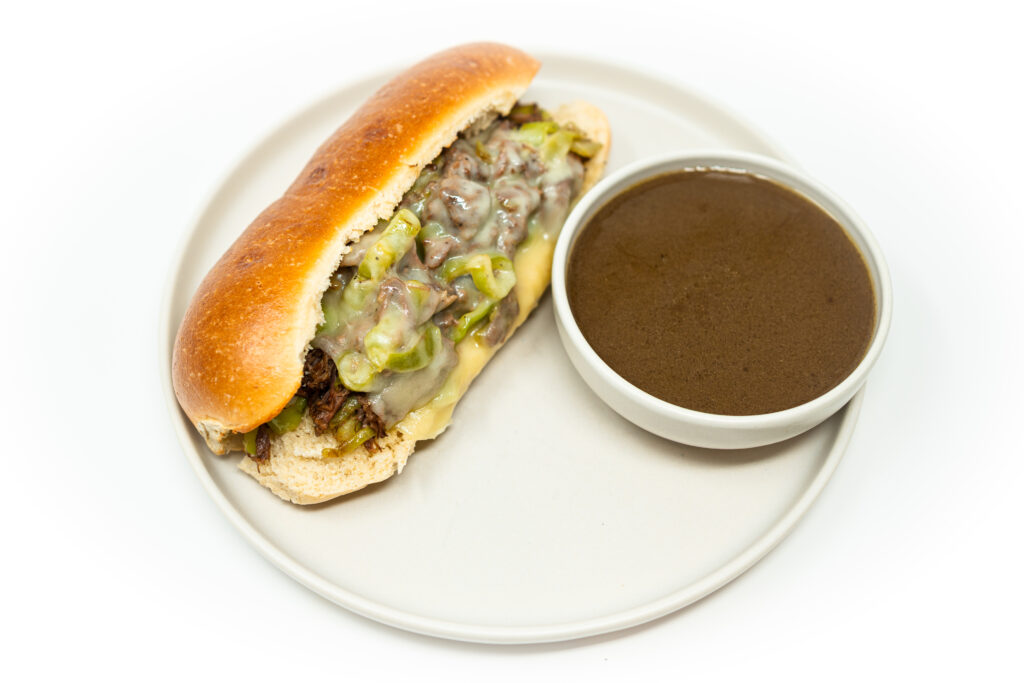 A beef short rib hoagie filled with tender, slow-cooked beef, sautéed Cubanelle peppers, and melted cheese, all nestled in a toasted hoagie roll, highlighting the savory filling and golden bread.