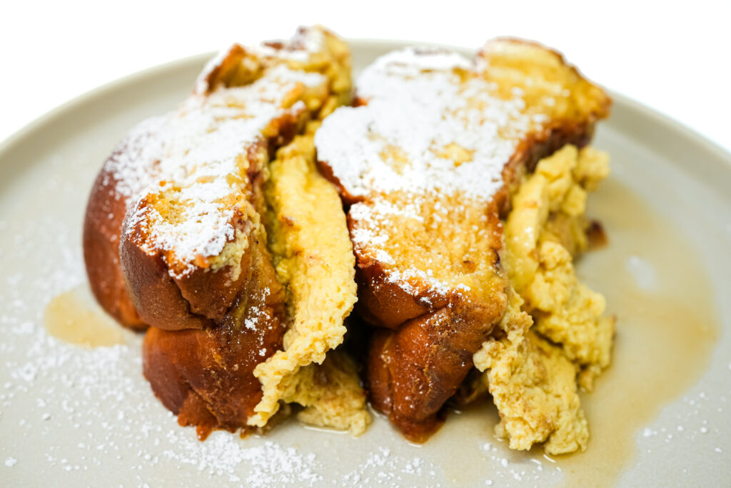 Golden Baked Challah French Toast served on a plate, featuring thick slices of challah bread baked until crispy on the outside and soft on the inside, dusted with powdered sugar for a rich, indulgent breakfast