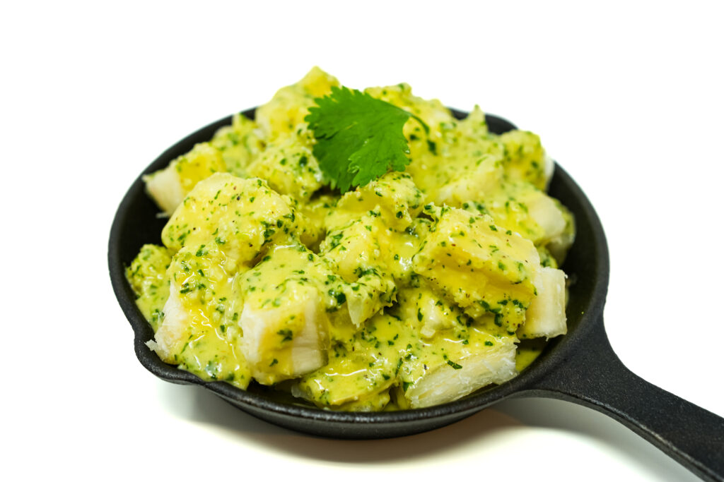 Yuca con Mojo served in a cast iron skillet, featuring tender boiled yuca drizzled with a tangy garlic-citrus mojo sauce, garnished with fresh herbs for a flavorful and rustic presentation
