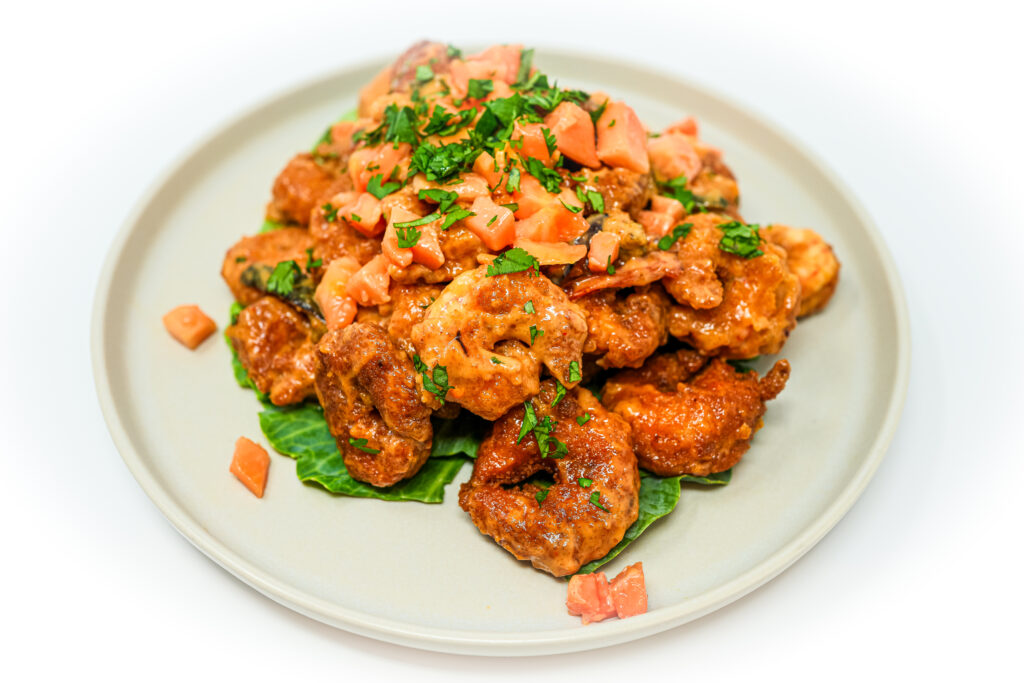 Tropical Papaya Bang Bang Shrimp served on a plate, featuring crispy fried shrimp tossed in a sweet and spicy papaya-infused sauce, offering a flavorful blend of tropical sweetness and a slight kick, garnished with fresh herbs.