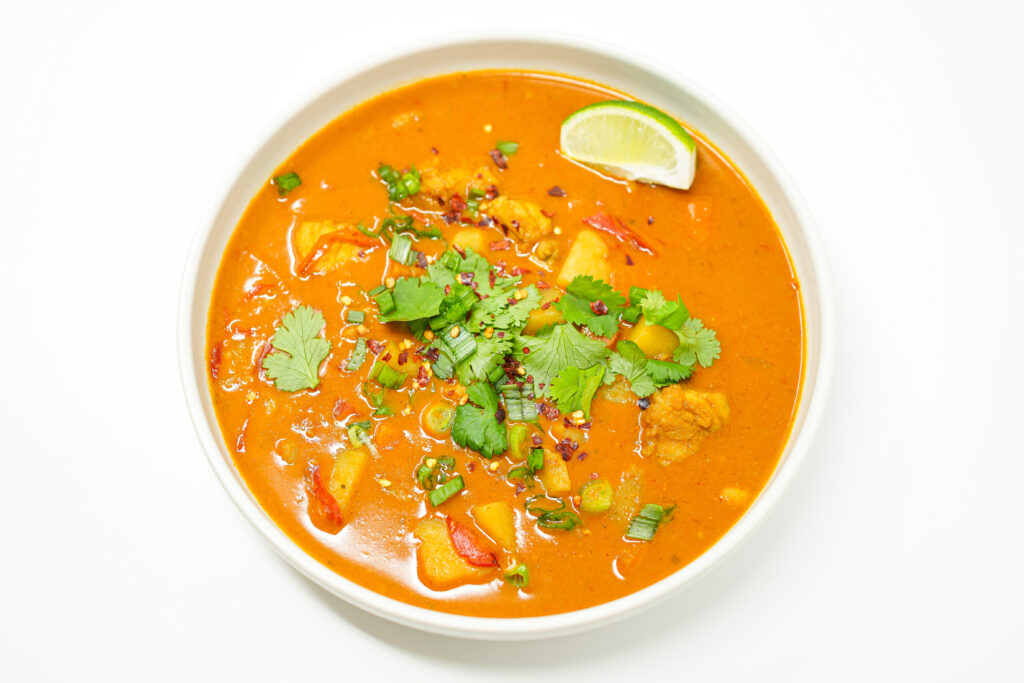 A bowl of creamy monkfish and potato curry, featuring tender chunks of fish and potatoes in a rich, golden sauce, garnished with fresh cilantro leaves and a lime wedge on the side for added brightness. The dish is vibrant and inviting, showcasing a delicious blend of textures and flavors.