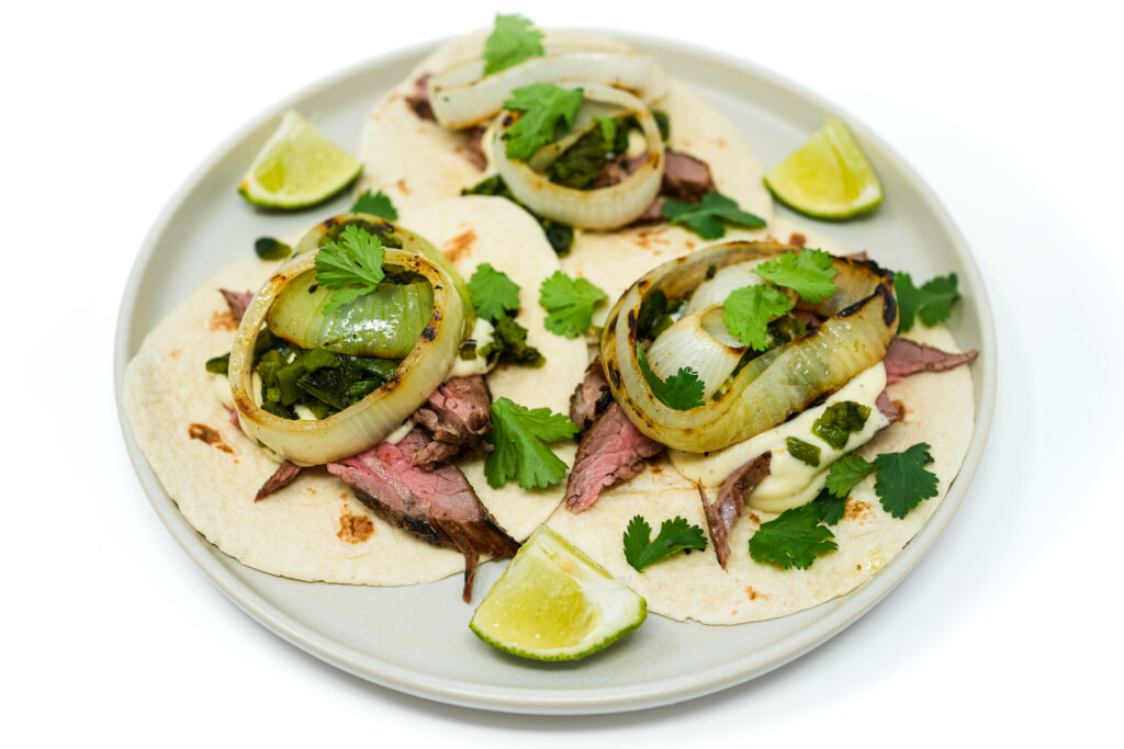 Grilled Flank Steak, Onion, and Poblano Pepper Fajitas served on a sizzling platter, featuring tender slices of marinated flank steak, charred onions, and smoky poblano peppers, ready to be wrapped in warm tortillas for a flavorful fajita experience