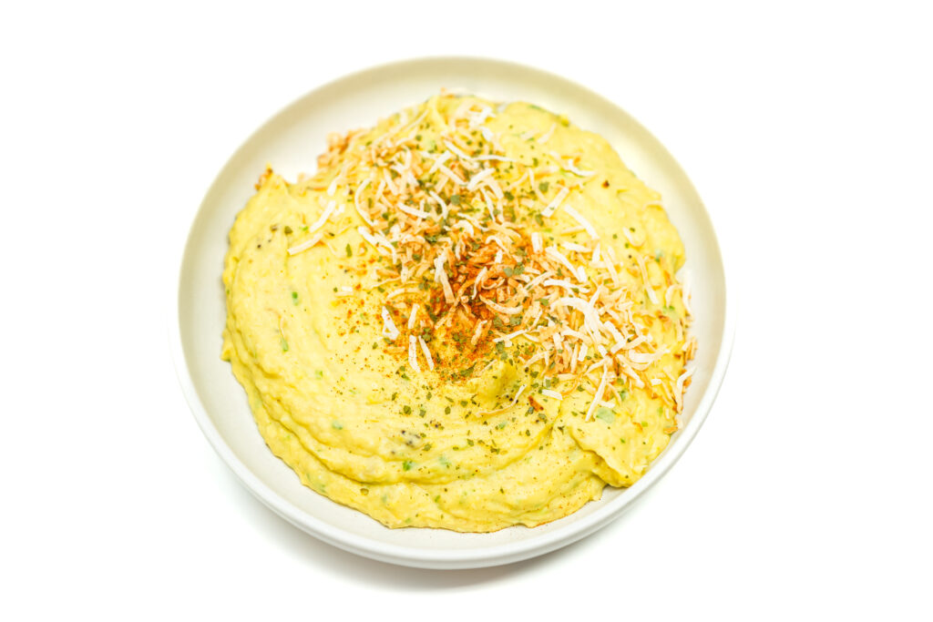 Mashed Caribbean Creamed Plantains garnished with chopped toasted coconut and paprika, showcasing the creamy texture of the plantains combined with vibrant green onions for a flavorful dish.