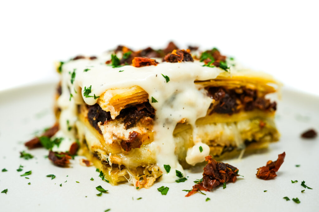 Artichoke, Brussels Sprouts, and Sun-Dried Tomato Lasagna served on a plate, featuring layers of tender pasta, creamy cheese, and a savory filling of artichokes, roasted Brussels sprouts, and tangy sun-dried tomatoes, baked to perfection