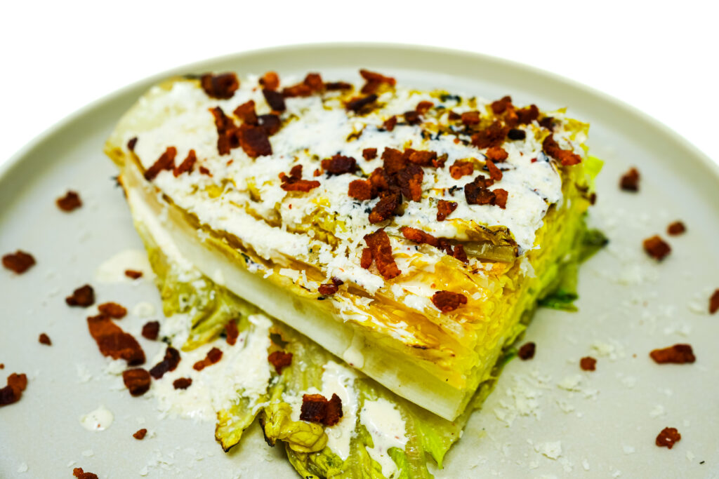 Grilled Caesar Salad served on a plate, featuring charred romaine lettuce drizzled with creamy homemade Caesar dressing, topped with shaved Parmesan and crispy bacon for a smoky, savory twist on the classic salad.