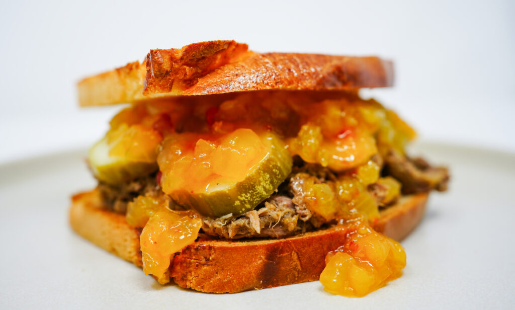 Pulled pork sandwich with Vidalia onion relish and pickles, featuring tender, smoky pulled pork topped with sweet caramelized Vidalia onions and tangy pickles, all served on a toasted bread