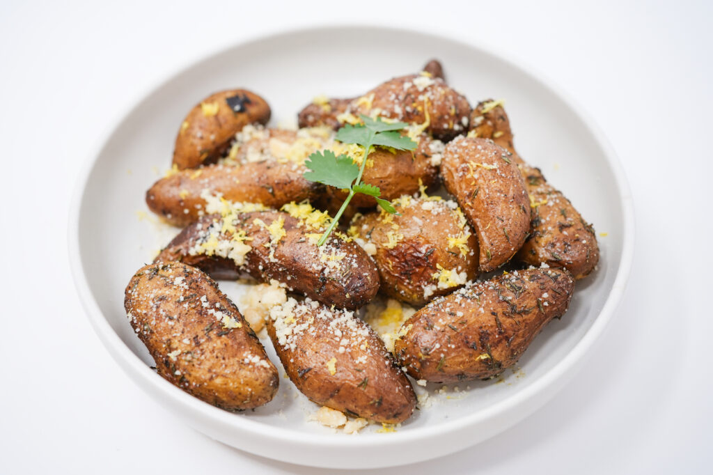 Smoked fingerling potatoes served on a plate, garnished with fresh lemon zest and grated Parmesan cheese, creating a smoky, citrusy, and savory dish