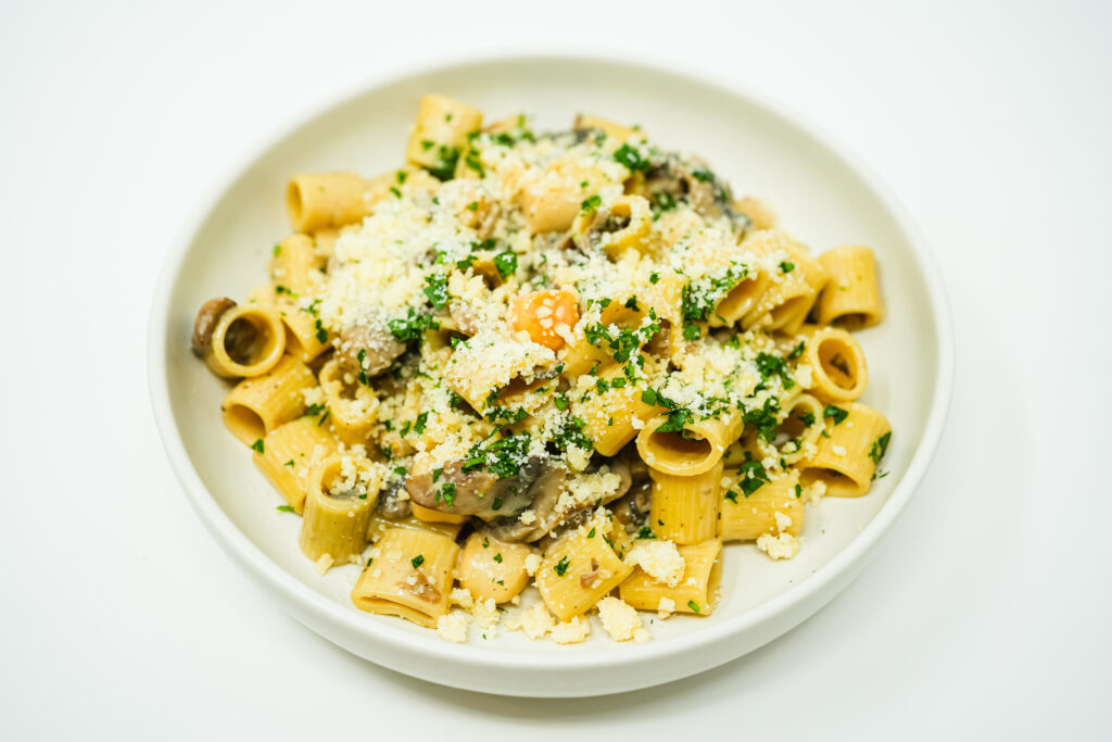 A bowl of Scallop and Mushroom Rigatoni Alfredo, featuring tender seared scallops, sautéed mushrooms, and rigatoni pasta coated in a creamy Alfredo sauce, garnished with fresh parsley and Parmesan.