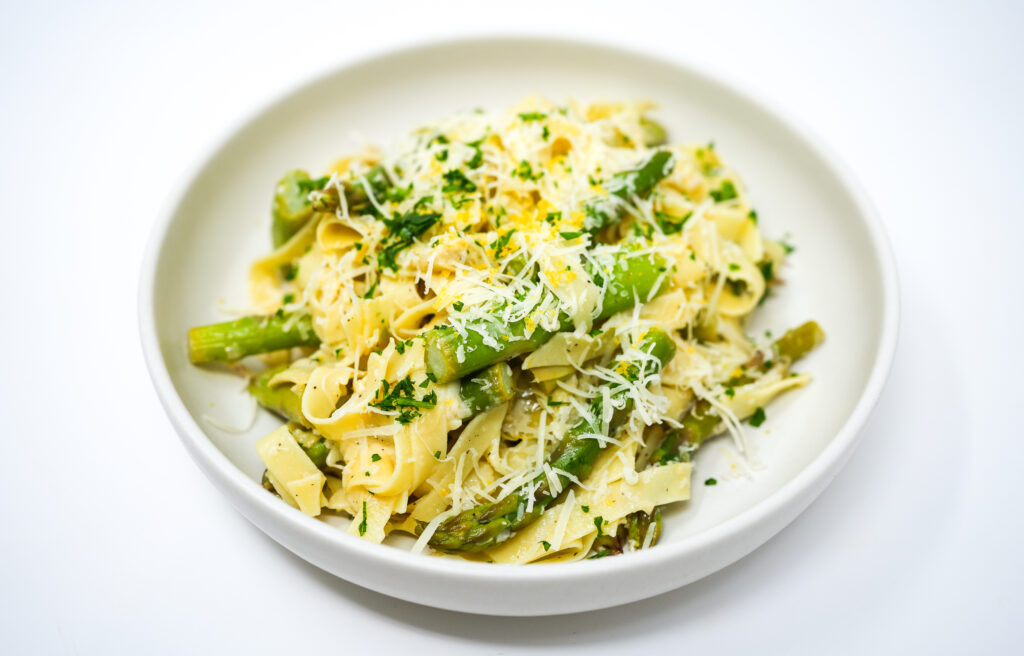 A close-up image of Artichoke, Asparagus, and Lemon Fettuccini, showcasing the vibrant green asparagus and artichoke pieces intertwined with lemon-zested noodles.