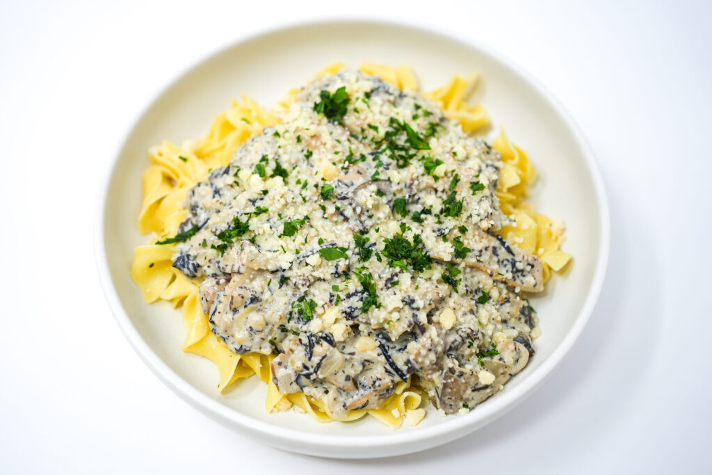 A creamy Wild Mushroom Stroganoff served in a white bowl, richly garnished with fresh chopped parsley, showcasing a variety of wild mushrooms in a thick, savory sauce.