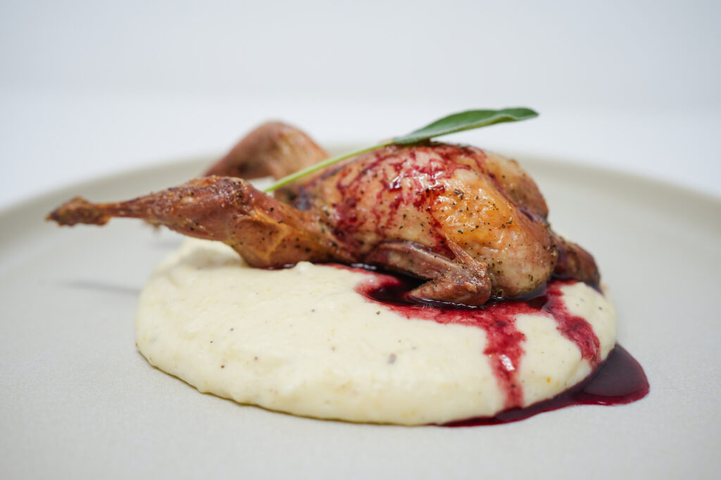 A beautifully plated Roasted Quail with a glossy Blackberry Sage Sauce drizzled over, highlighting the dish's elegant presentation and inviting colors.