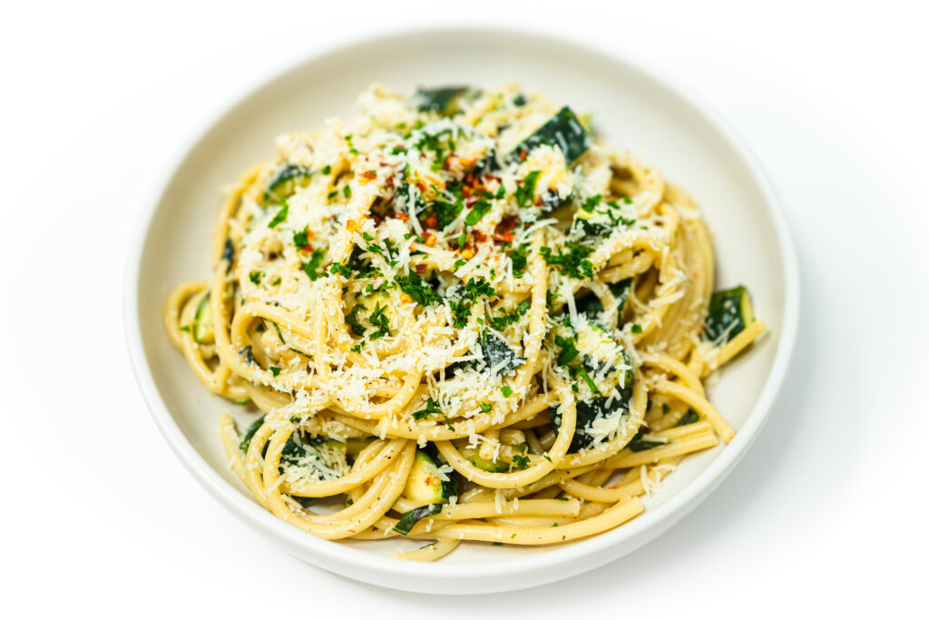 A plate of Grilled Zucchini Bucatini Alfredo featuring creamy, white sauce-coated bucatini noodles interspersed with slices of smoky grilled zucchini, garnished with fresh parsley and a sprinkle of Parmesan cheese.