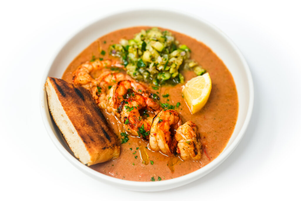 A colorful plate of Grilled Royal Red Shrimp over vibrant heirloom tomato gazpacho, accompanied by a fresh grilled zucchini salsa and a side of lightly charred naan bread, showcasing a harmonious blend of fresh summer flavors and textures.