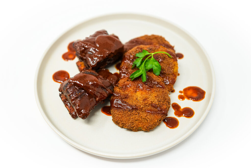 A plate of Southern-Inspired Braised Beef Short Ribs and Fried Green Tomatoes, showcasing tender, slow-cooked ribs draped in a rich, glossy sauce alongside golden-brown, crispy fried green tomatoes, embodying a hearty and flavorful Southern meal.