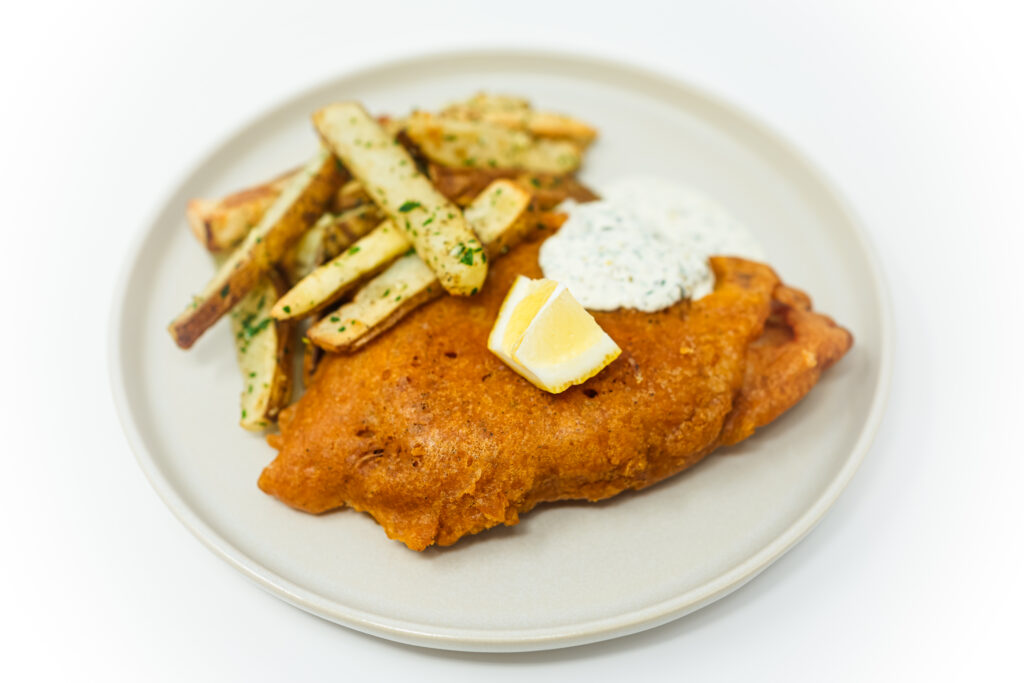 Crispy beer-battered fish with garlic parsley fries and homemade tartar sauce on a white plate.