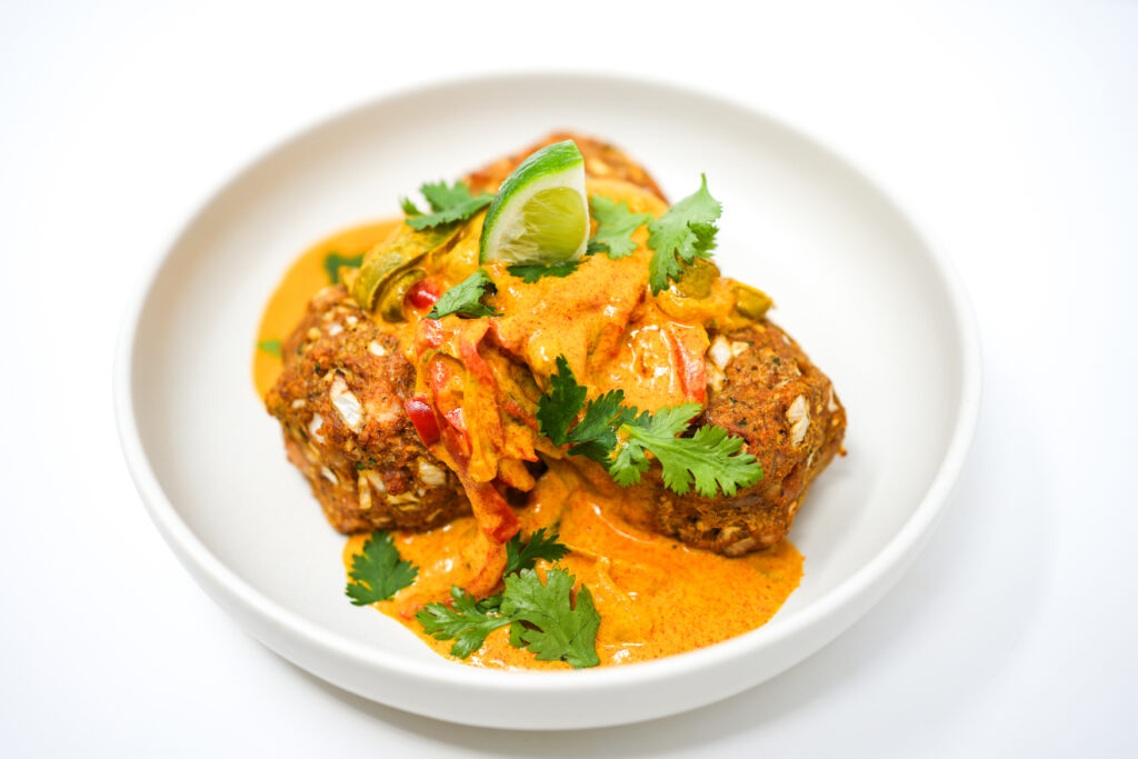 A warm, inviting dish of Coconut Curry Chicken Meatballs, featuring golden-brown meatballs nestled in a rich, creamy coconut curry sauce, garnished with fresh cilantro and a lime wedge.