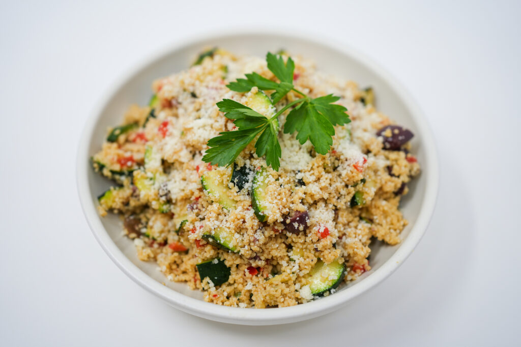 Colorful Grilled Zucchini Couscous Salad with vibrant vegetables and herbs, served in a bowl on a clean white background.