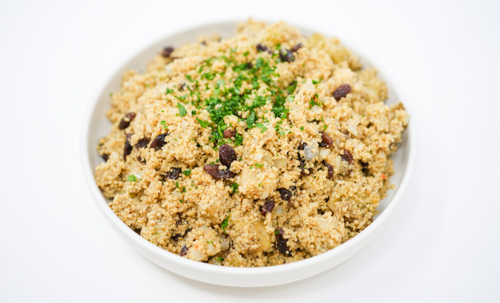 A colorful dish of Mediterranean Roasted Eggplant and Raisin Couscous with Toasted Pine Nuts, showcasing golden couscous, deep purple eggplant, glistening raisins, and golden-brown pine nuts, garnished with fresh green herbs.