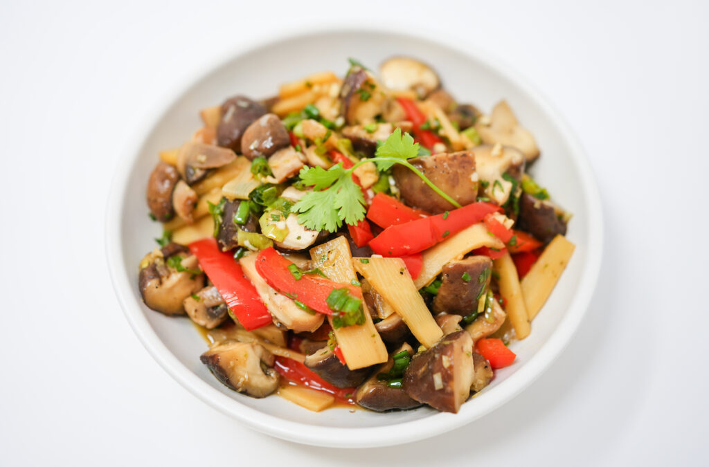 A colorful Sesame Soy Shiitake Mushroom Salad featuring quartered shiitake mushrooms, slices of red bell pepper, bamboo shoots, and onion, all tossed with a glossy, cilantro-infused sesame soy dressing.