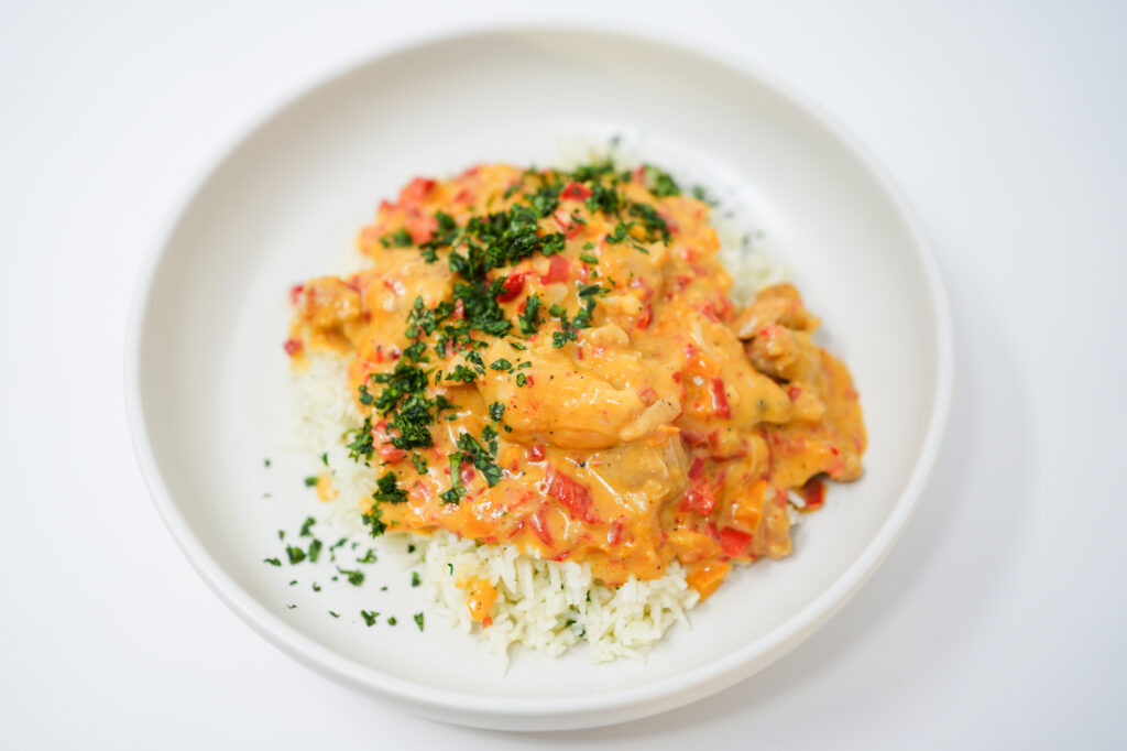 A serving of Passionfruit Coconut Chicken featuring golden-brown chicken thighs nestled in a creamy, pale orange sauce made from passionfruit and coconut milk, garnished with vibrant green cilantro, served over a bed of fluffy white basmati rice.