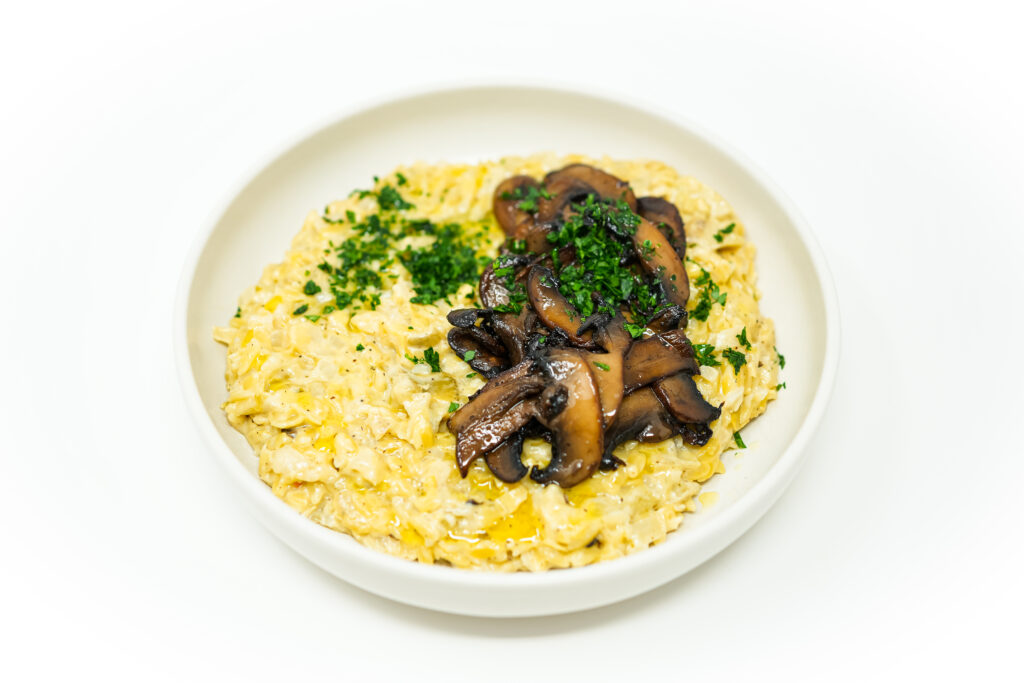A bowl of creamy orzo pasta mixed with artichoke hearts, topped with golden-brown caramelized mushrooms, and garnished with fresh parsley.