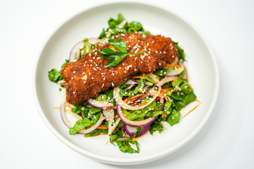 A vibrant dish featuring golden, crispy monkfish pieces on a fresh salad of chopped romaine, julienned carrot, thinly sliced red onion, and basil, all drizzled with a sweet chili vinaigrette and garnished with sesame seeds.