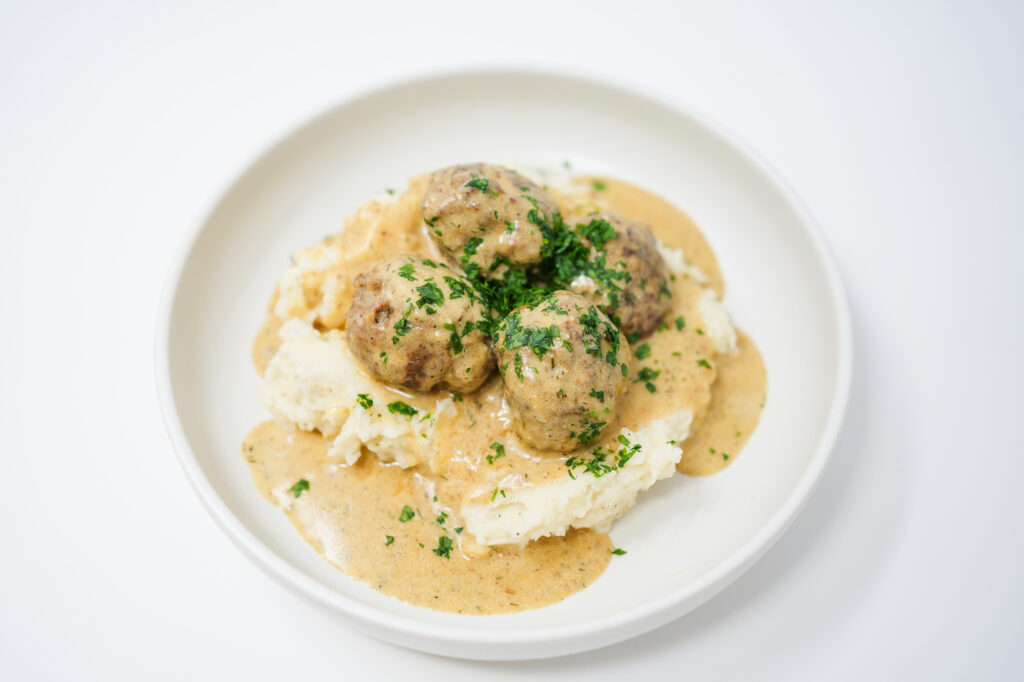 A plate of Creamy Dill Swedish Meatballs served over fluffy mashed potatoes, topped with a rich, herb-infused cream sauce and garnished with fresh parsley.