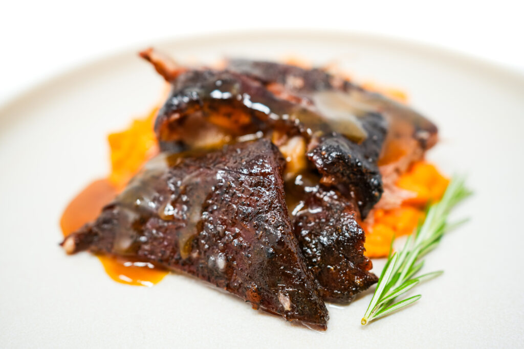 A beautifully caramelized Honey Mustard Roasted Lamb Breast served atop paprika mashed sweet potatoes, garnished with fresh herbs.