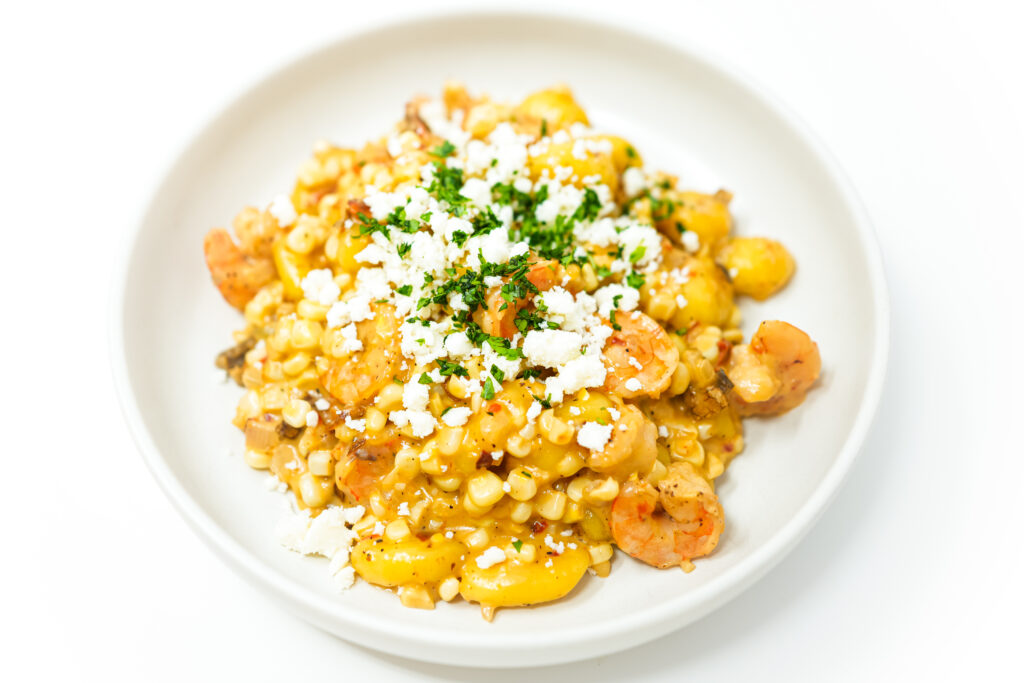A bowl of Creamy Shrimp, White Corn, and Chipotle Gnocchi featuring tender shrimp, sweet corn, and gnocchi in a rich cream sauce, garnished with fresh basil and crumbled queso fresco.