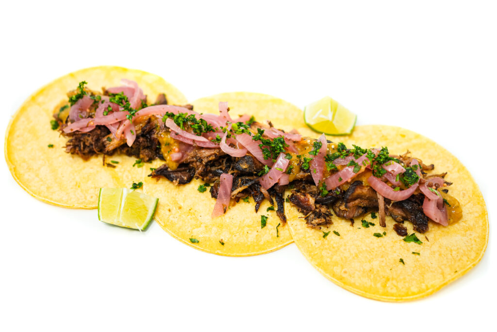 A plate of Pork Carnitas Bell Pepper Salsa Verde Tacos featuring tender pork, vibrant green salsa, and tangy pickled onions, garnished with fresh cilantro and lime wedges, served on warm corn tortillas.