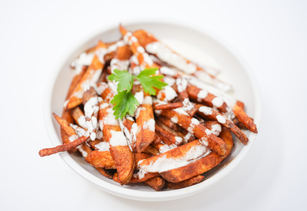A plate of crispy, golden-brown paprika steak fries garnished with fresh parsley, served alongside a bowl of creamy, tangy passionfruit aioli. The vibrant colors and textures highlight the unique combination of smoky and tropical flavors.