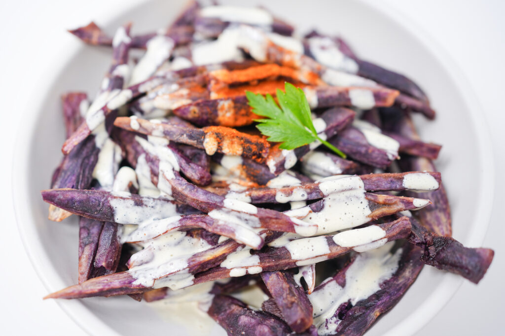 A plate of crispy ube fries drizzled with creamy mango aioli, garnished with chili powder.