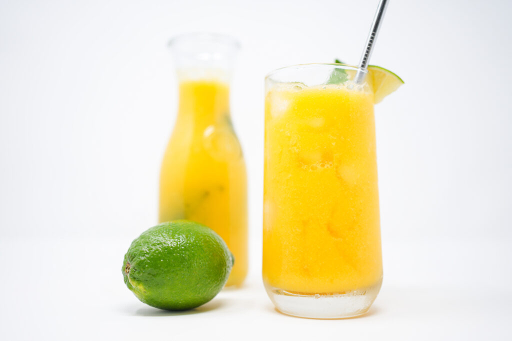 A refreshing glass of Basil Mango Agua Fresca, garnished with fresh basil leaves and a wedge of lime, featuring a bright yellow-orange color and served over ice cubes.
