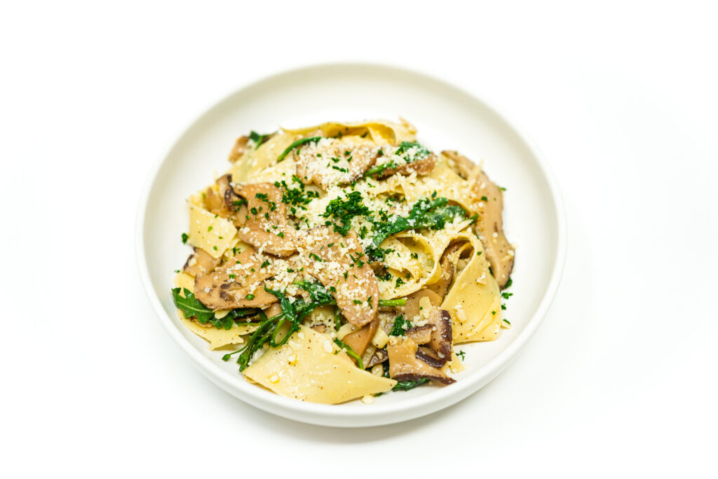 A serving of Garlic Shiitake Pappardelle with Fresh Arugula, showcasing wide pasta ribbons, earthy mushrooms, and vibrant greens in a light Parmesan sauce.