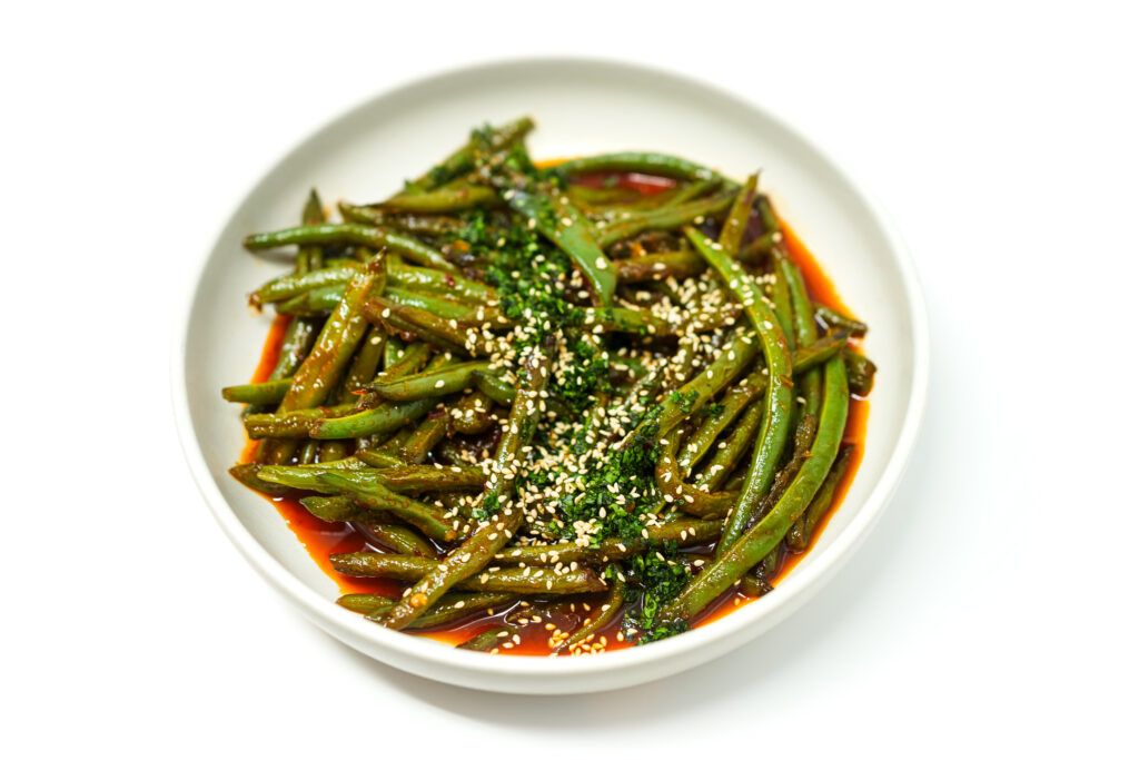 A plate of Szechuan Stir-Fried Green Beans garnished with toasted sesame seeds and fresh cilantro, showcasing vibrant green beans coated in a rich, spicy chili-garlic sauce