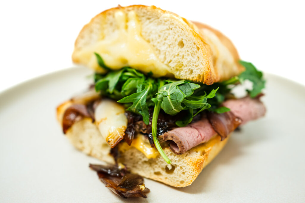A gourmet roast beef sandwich with tender slices of roast beef, sweet and tangy caramelized shallots, creamy Swiss cheese, and fresh arugula on a toasted roll.
