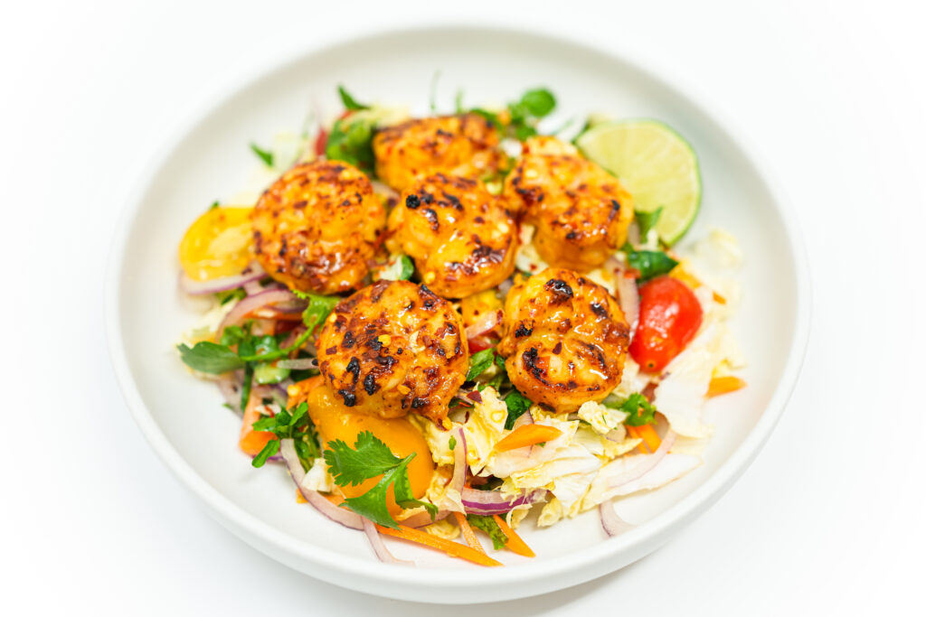 A vibrant plate of Grilled Chili-Lime Shrimp and Napa Cabbage Salad with grilled shrimp, Napa cabbage, watercress, cherry tomatoes, cilantro, carrot, and red onion, drizzled with lime vinaigrette and garnished with lime wedges.