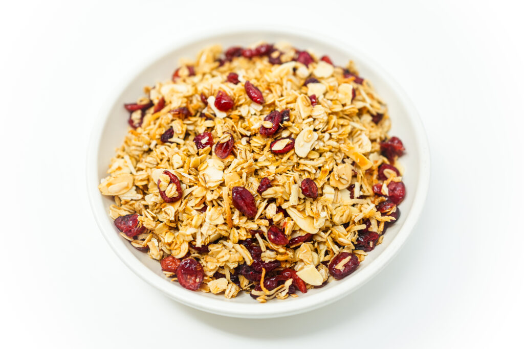 A bowl of Cranberry Coconut Almond Granola featuring rolled oats, dried cranberries, shredded coconut, and sliced almonds on a white background.