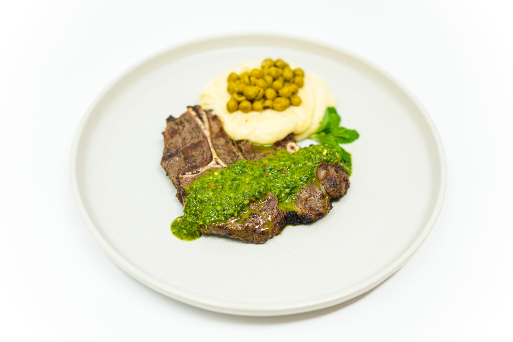 A plate of Grilled Lamb Steaks with Mint Chimichurri, Whipped Potatoes, and Sautéed Peas, garnished with fresh mint.