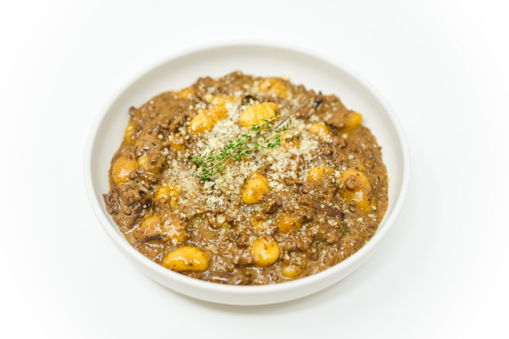 A plate of creamy gnocchi topped with ground beef and porcini mushrooms in a rich sauce, garnished with grated Parmesan cheese.
